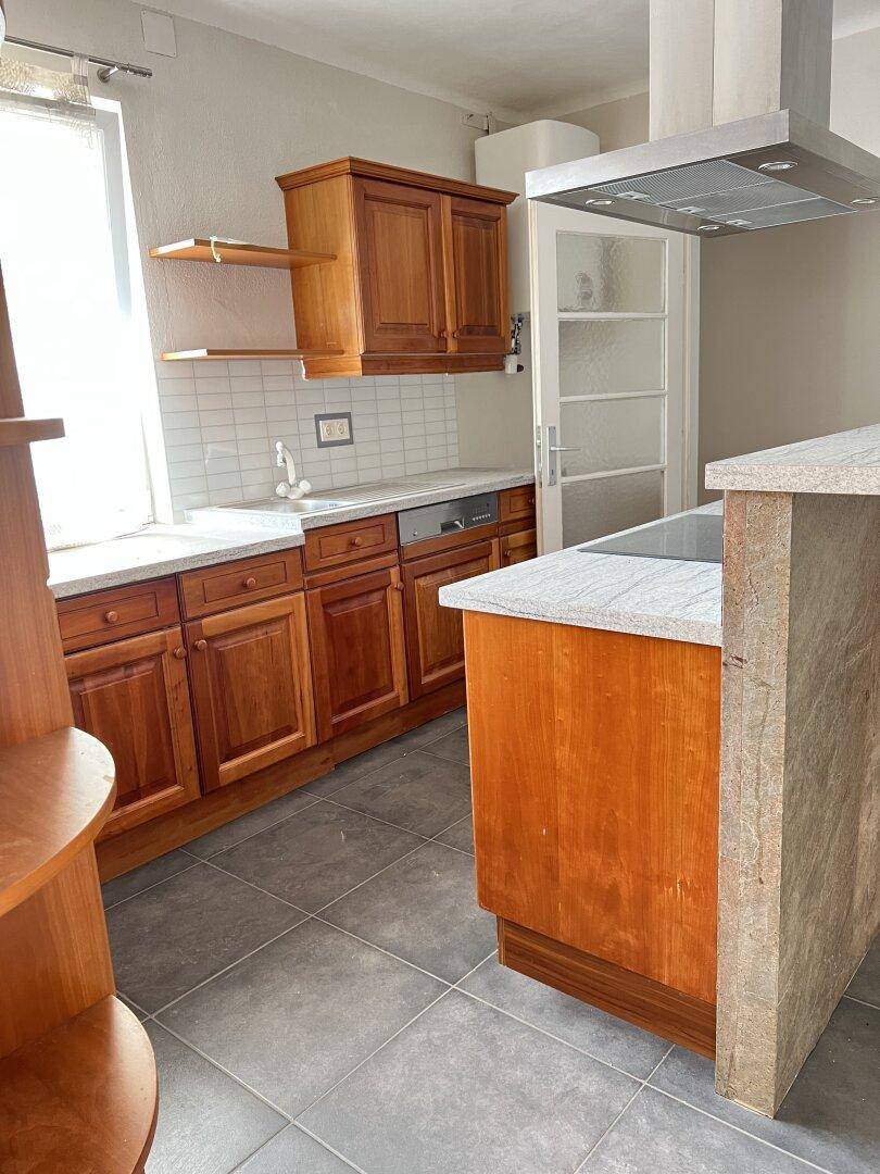 Helle Küche mit Holzfronten, Spüle, Geschirrspüler und Fenster, ergänzt durch eine weiße Fliesenrückwand.