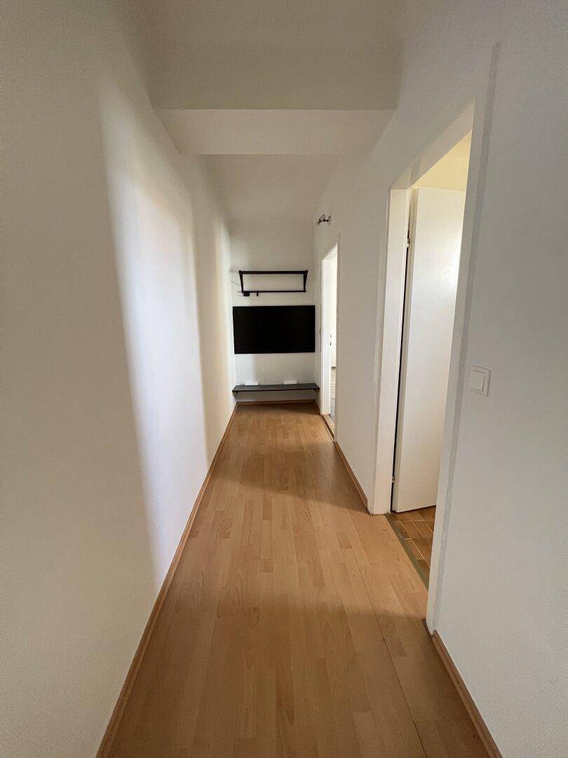 Langer, heller Flur mit Laminatboden und weißen Wänden, der zu weiteren Räumen führt.