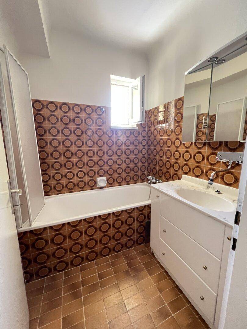 Badezimmer im 80er-Jahre-Stil mit Badewanne, Duschwand, Waschbecken und braun gemusterten Fliesen.