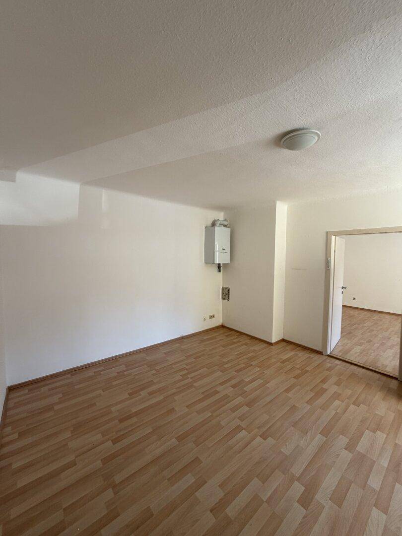 Leerer Raum mit Laminatboden und an der Wand montiertem Heizkessel, ideal als Hauswirtschaftsraum.