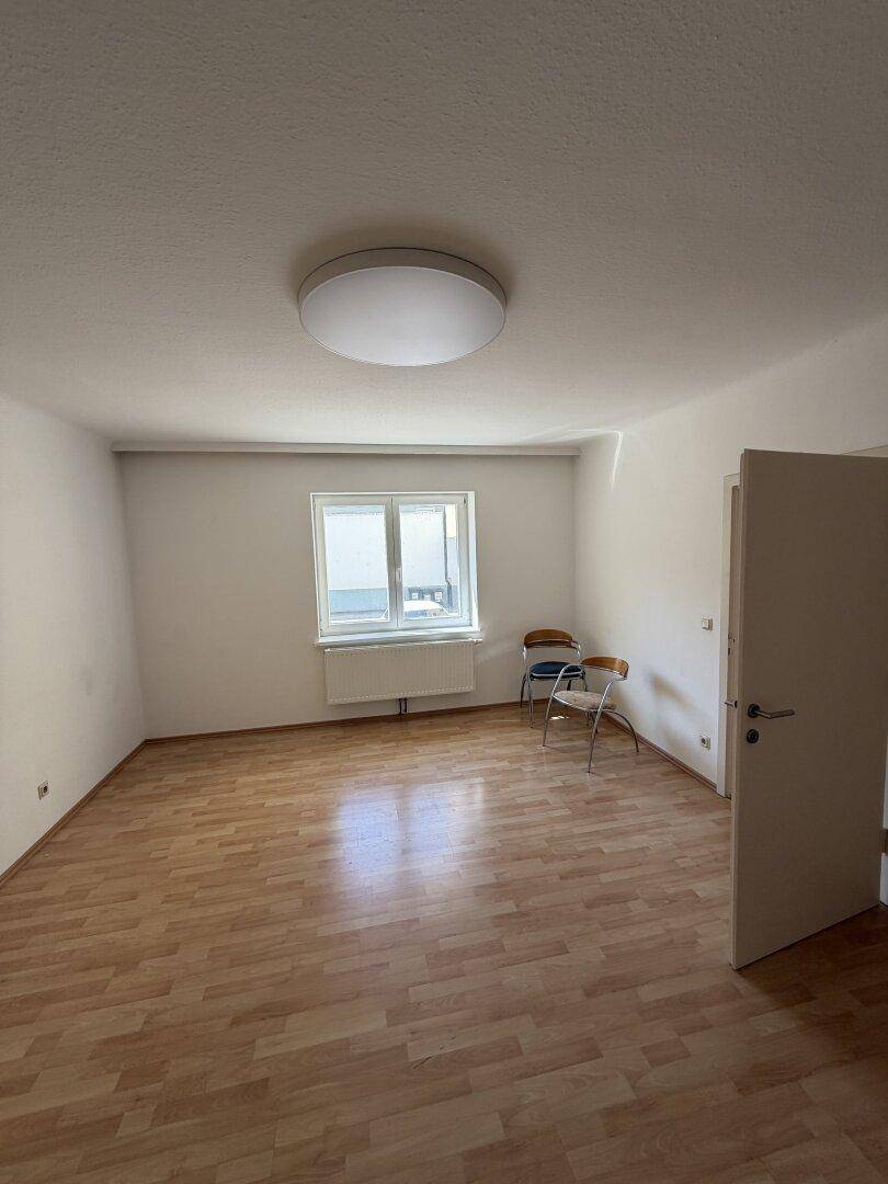 Helles, leeres Zimmer mit Laminatboden und großem Fenster, vielseitig nutzbar als Wohn- oder Schlafzimmer.
