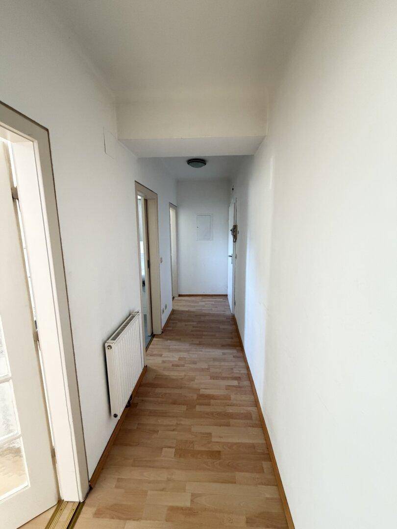 Langer, heller Flur mit Laminatboden und Heizkörper, der zu weiteren Räumen führt.