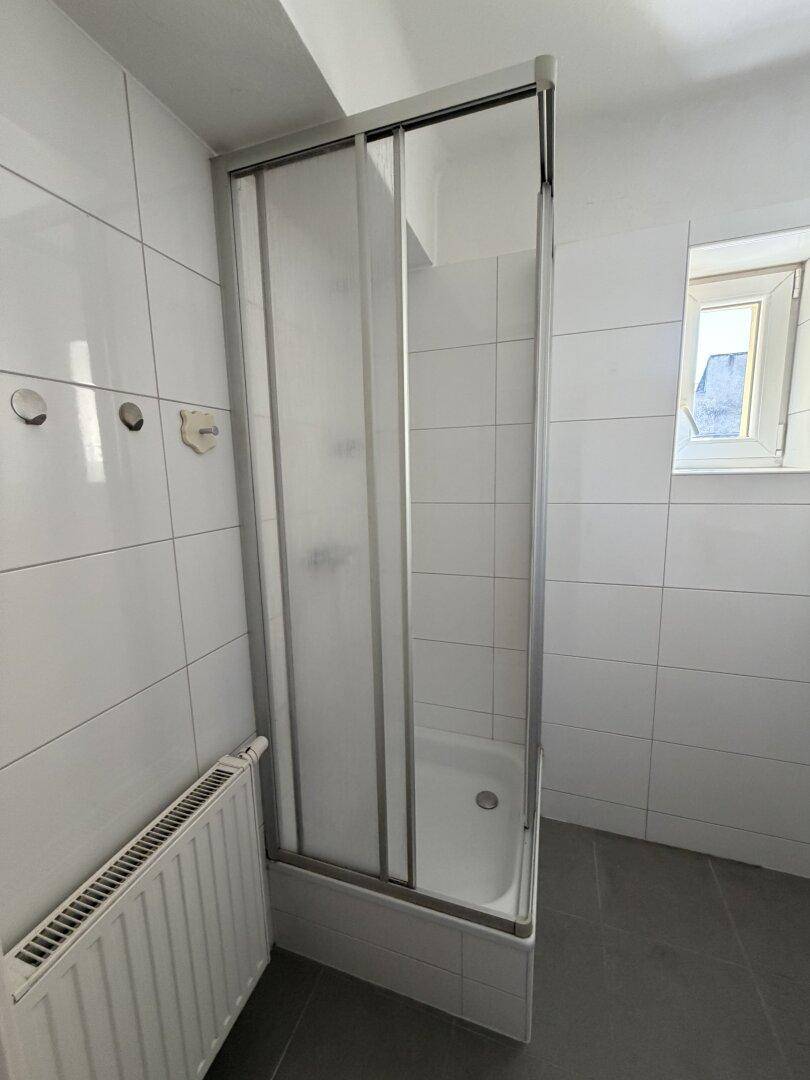 Badezimmer mit Dusch-Badewannen-Kombination, weißen Fliesen und Fenster für natürliche Belüftung.