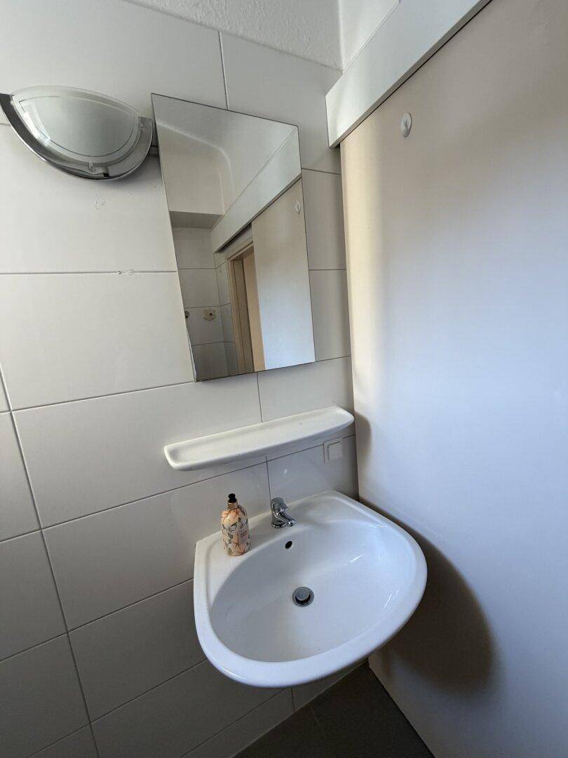 Badezimmer mit Waschbecken, Spiegel und weißen Wandfliesen, praktisch und hell gestaltet.