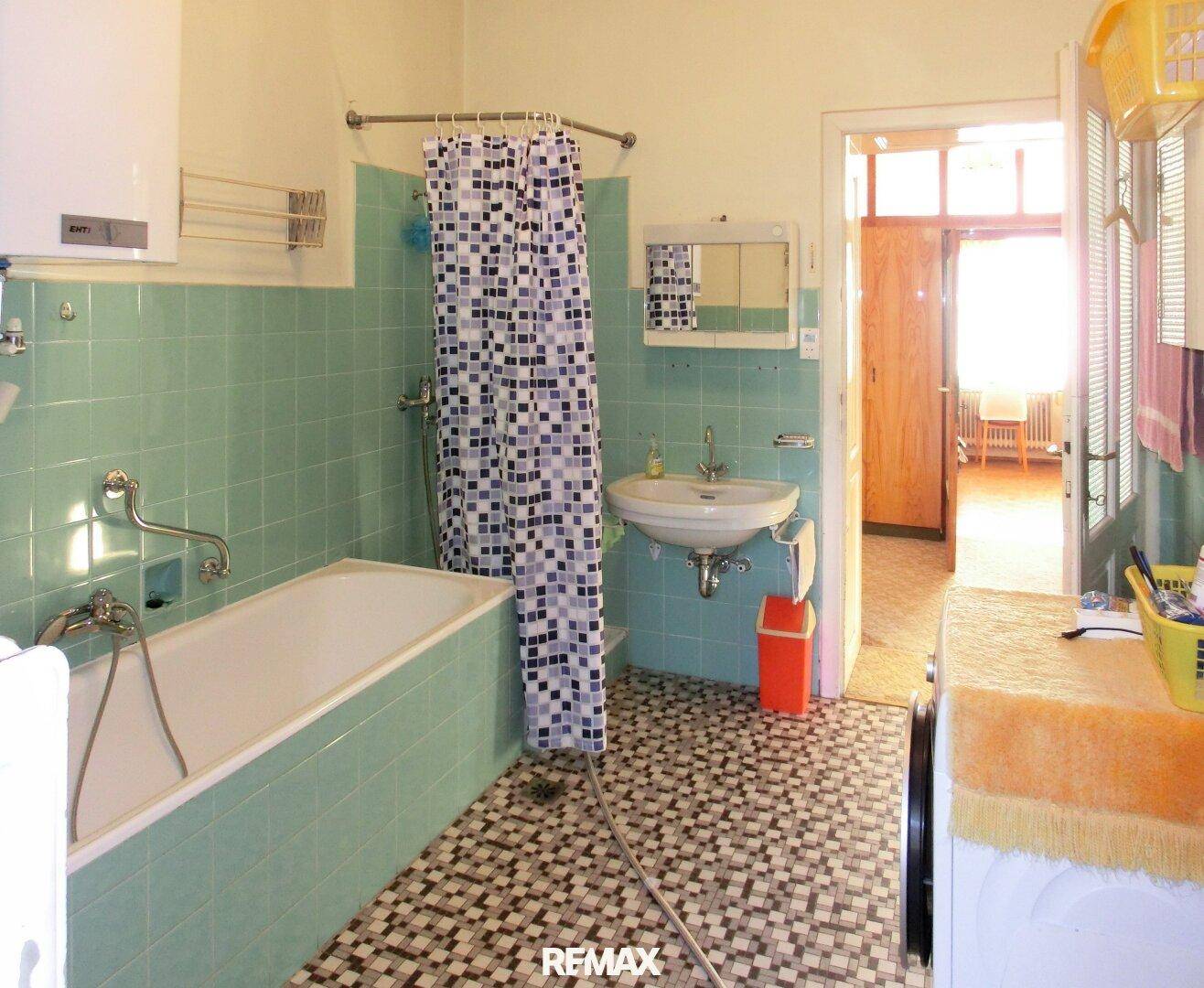 Badezimmer im Stil der 80er Jahre mit Badewanne, Duschvorhang und grünen Fliesen.