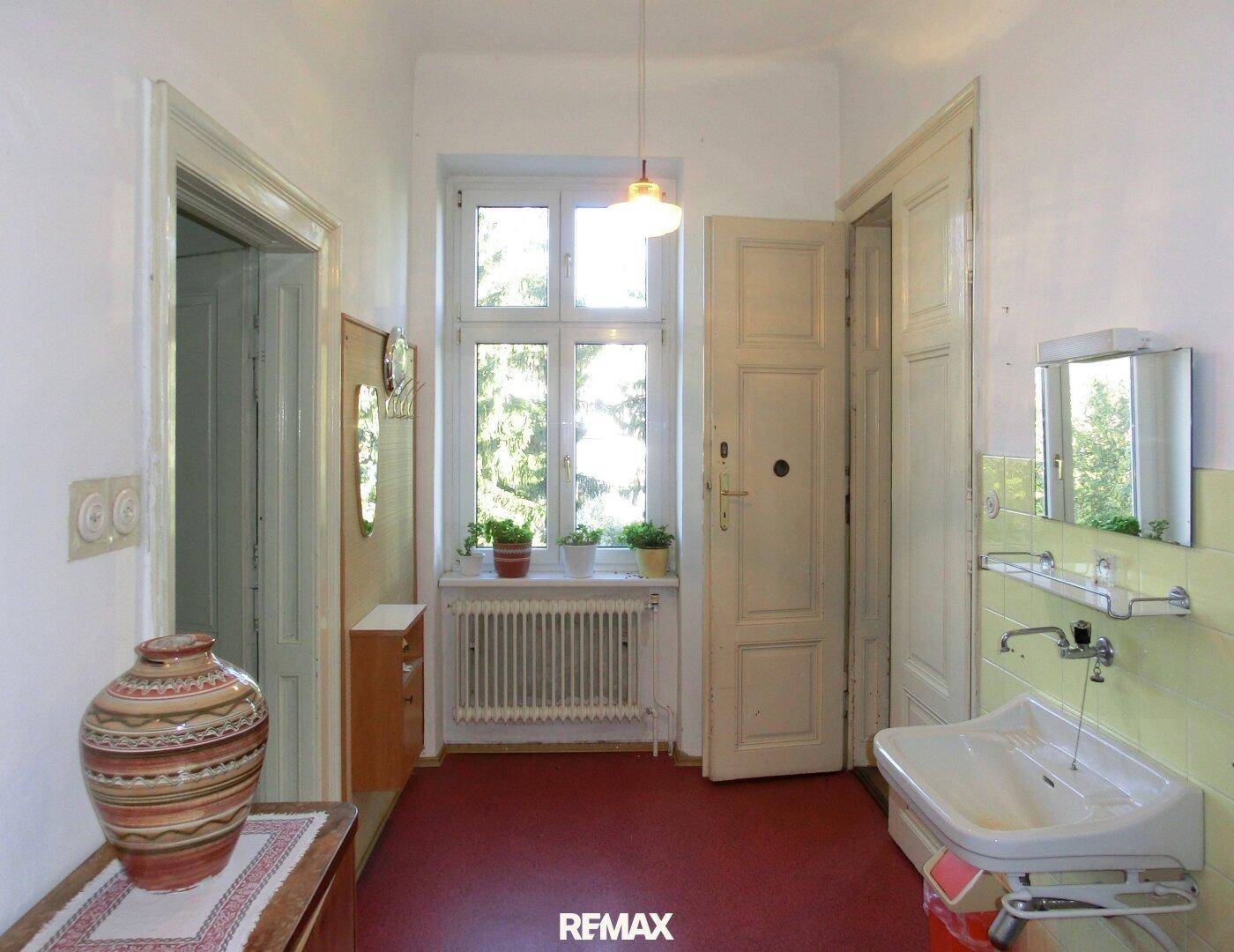 Raum mit Waschbecken, Fenster und rotem Bodenbelag, möglicherweise ein Hauswirtschaftsraum.