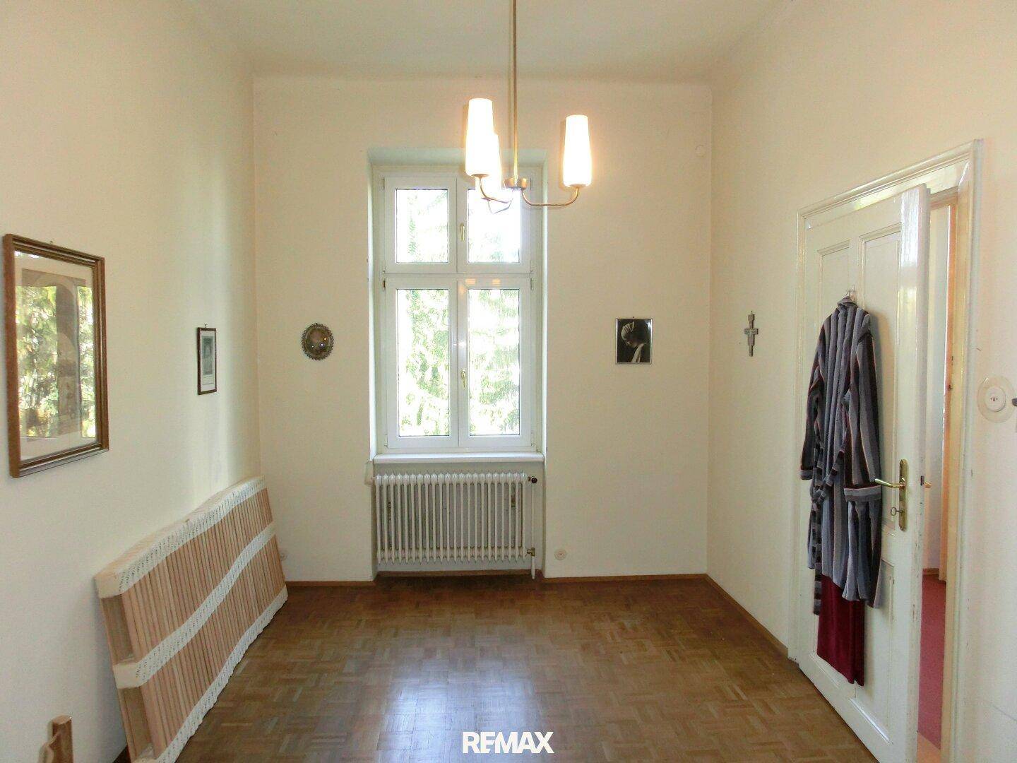 Leerer Raum mit Parkettboden, großem Fenster und einfacher Beleuchtung.