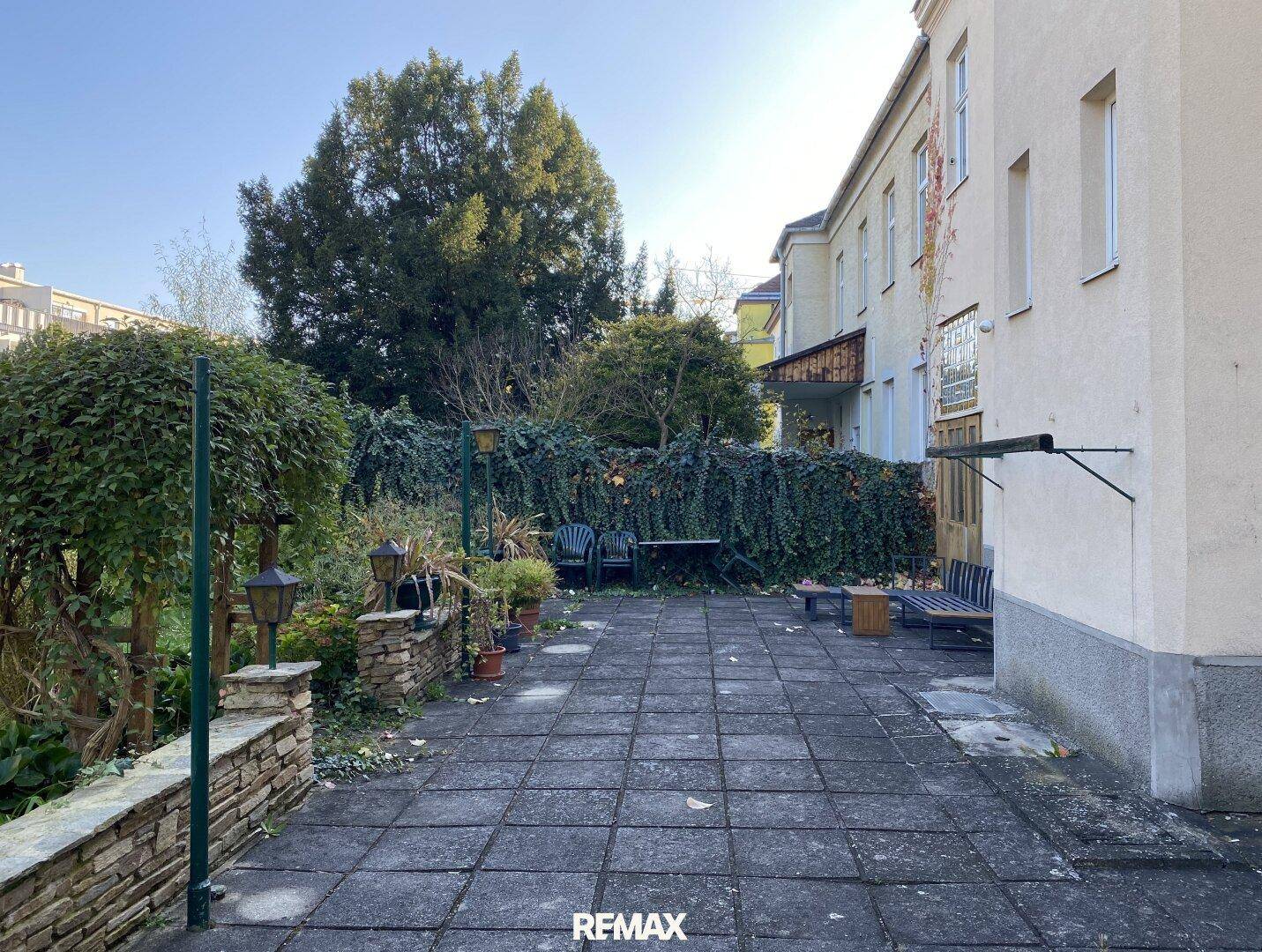 Gepflasterte Terrasse im Gartenbereich mit Sitzgelegenheiten und Hecken.