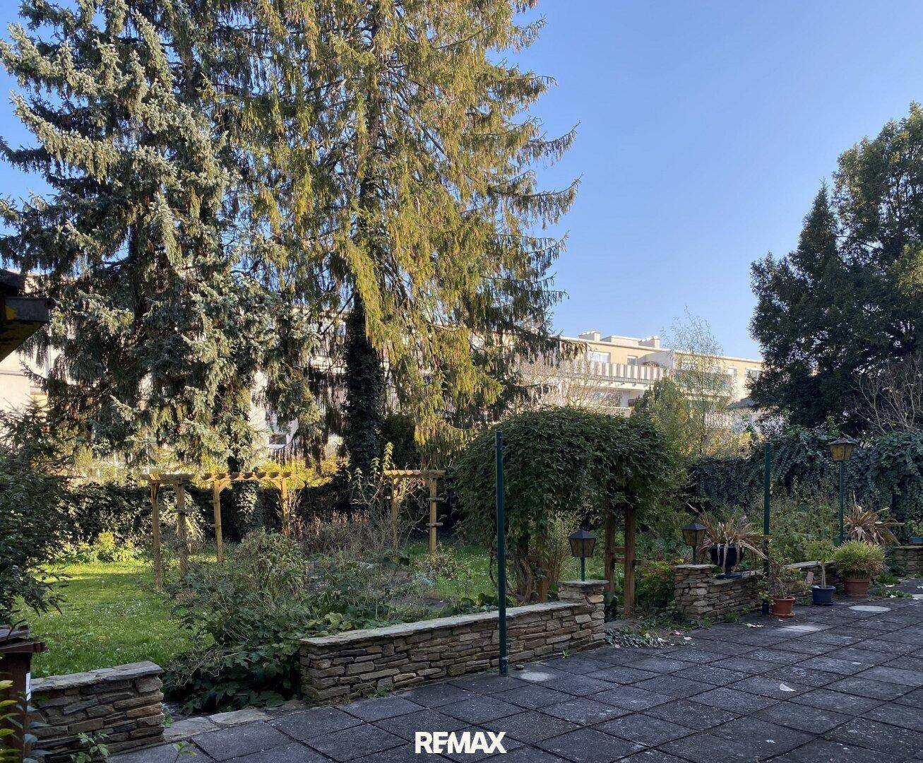 Große gepflasterte Terrasse mit Blick auf den grünen Garten und hohe Bäume.