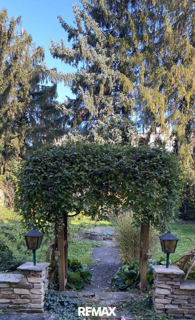 Gartenweg mit dekorativen Laternen, umgeben von Bäumen und Sträuchern.