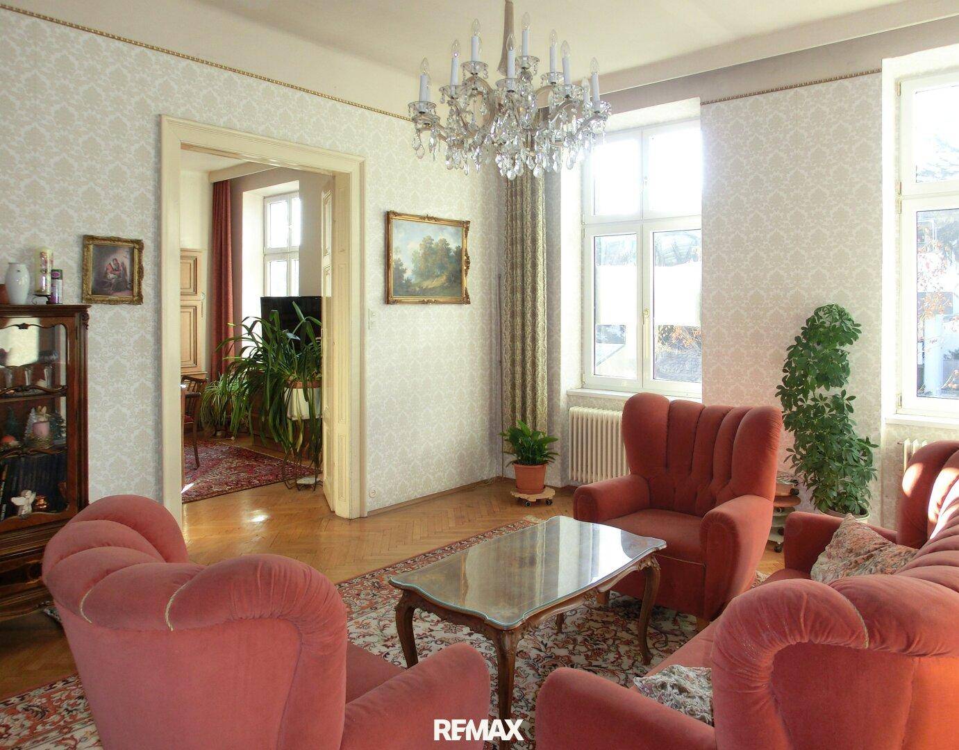 Helles Wohnzimmer mit traditionellen Möbeln, Kronleuchter und Blick ins Grüne.