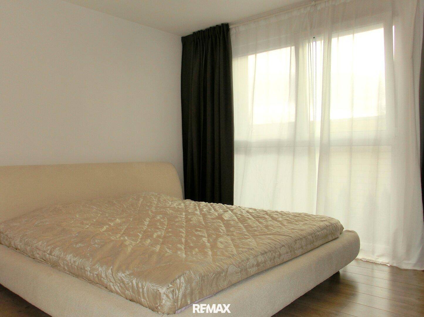 Schlafzimmer mit großem Bett, dunklen Vorhängen und viel Tageslicht.