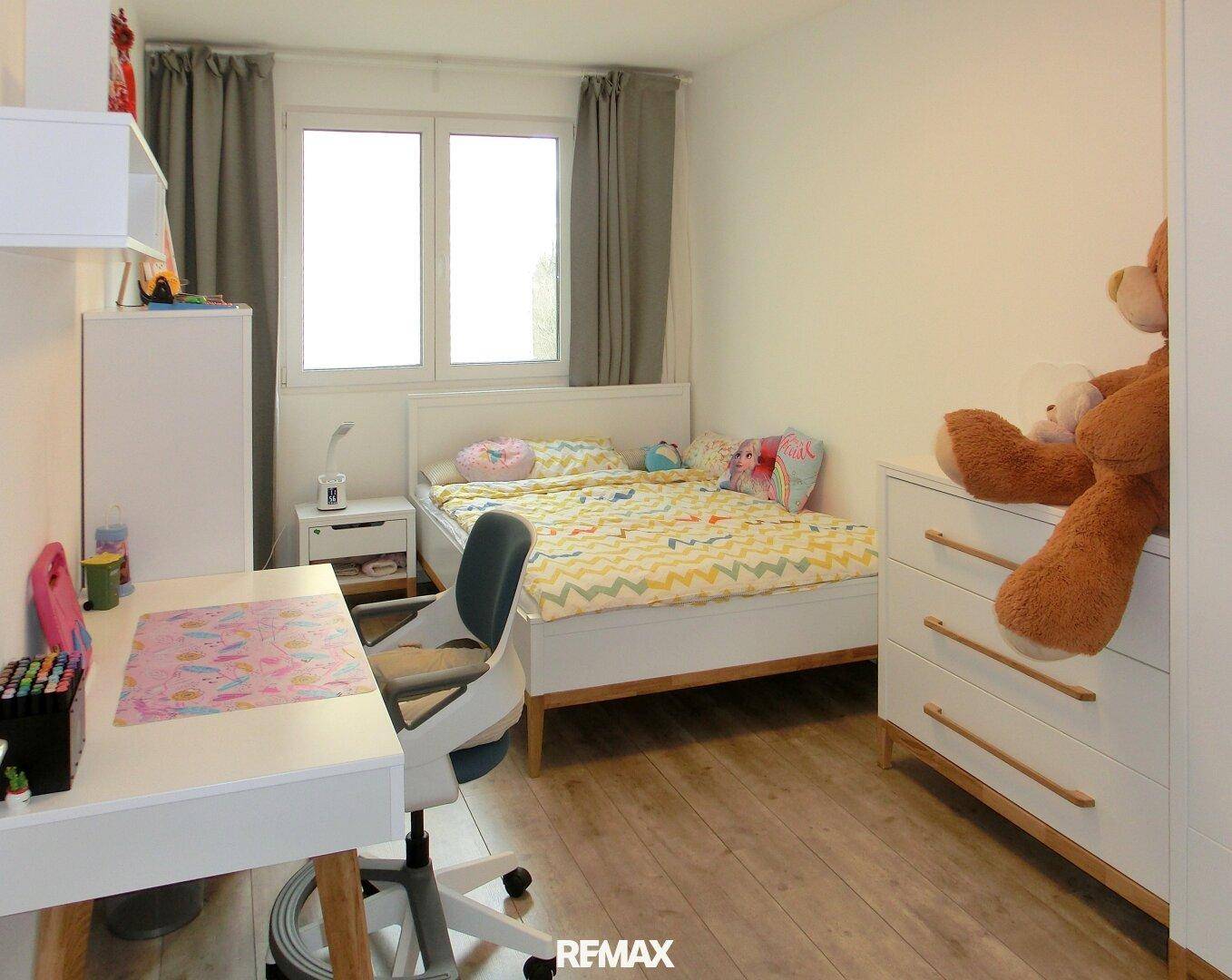 Helles Kinderzimmer mit Schreibtisch, Bett und Laminatboden.