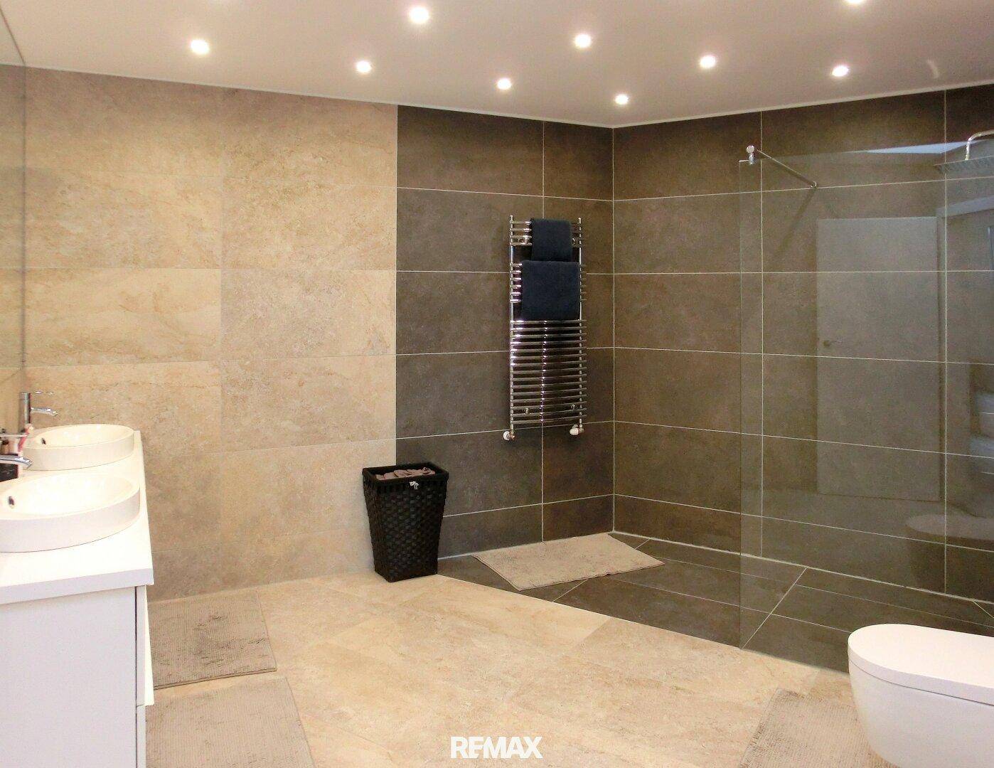 Modernes Badezimmer mit Doppelwaschbecken, großer Dusche und Fliesenboden.