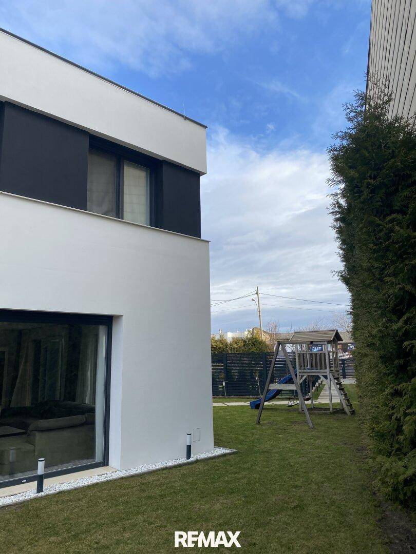 Seitenansicht des Hauses mit Rasenfläche und Kinderspielplatz.