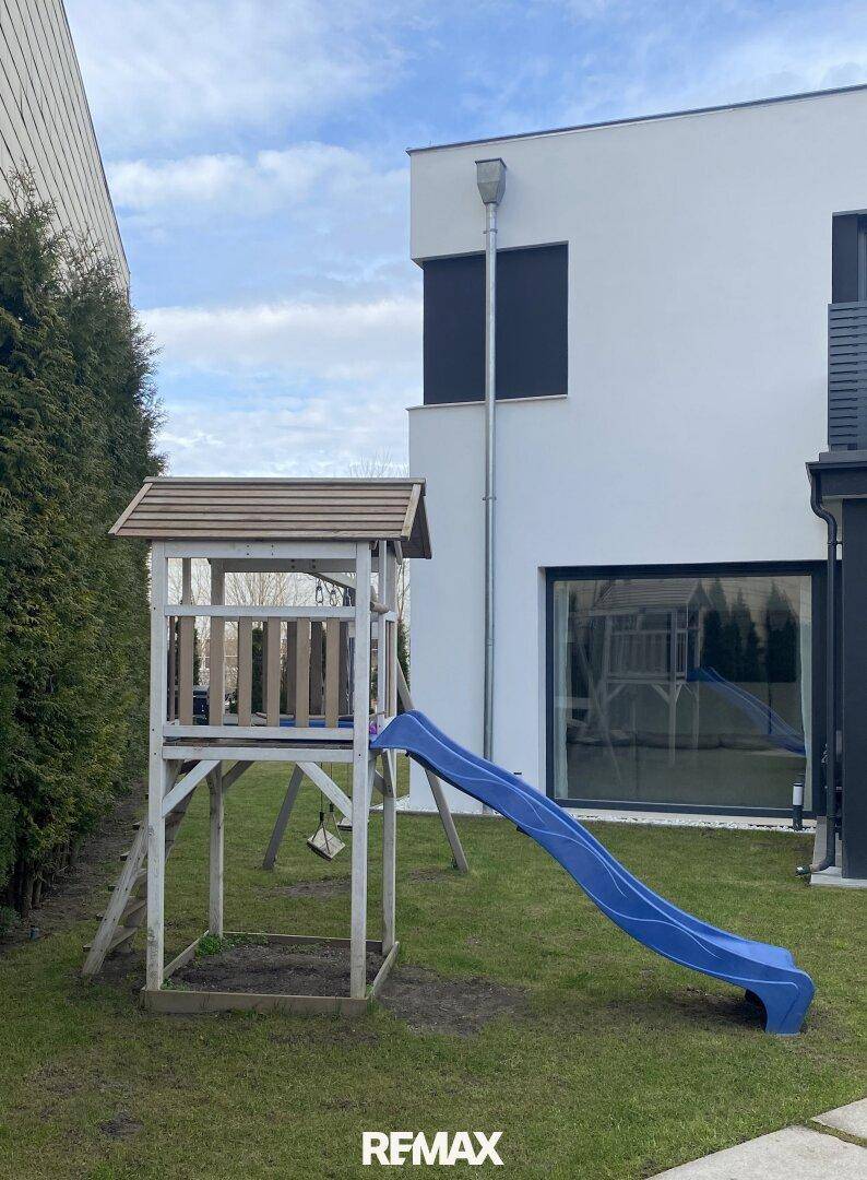 Moderner Garten mit Spielplatz, Rutsche und Spielturm neben dem Haus.
