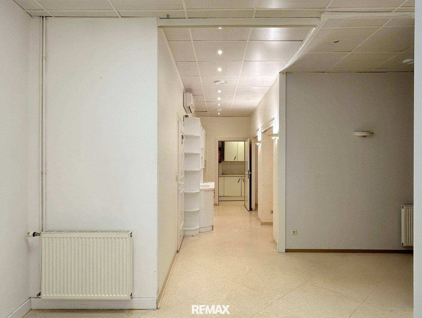 Langer Flur mit heller Beleuchtung und Heizkörper, der zu weiteren Räumen führt, mit abgehängter Decke.
