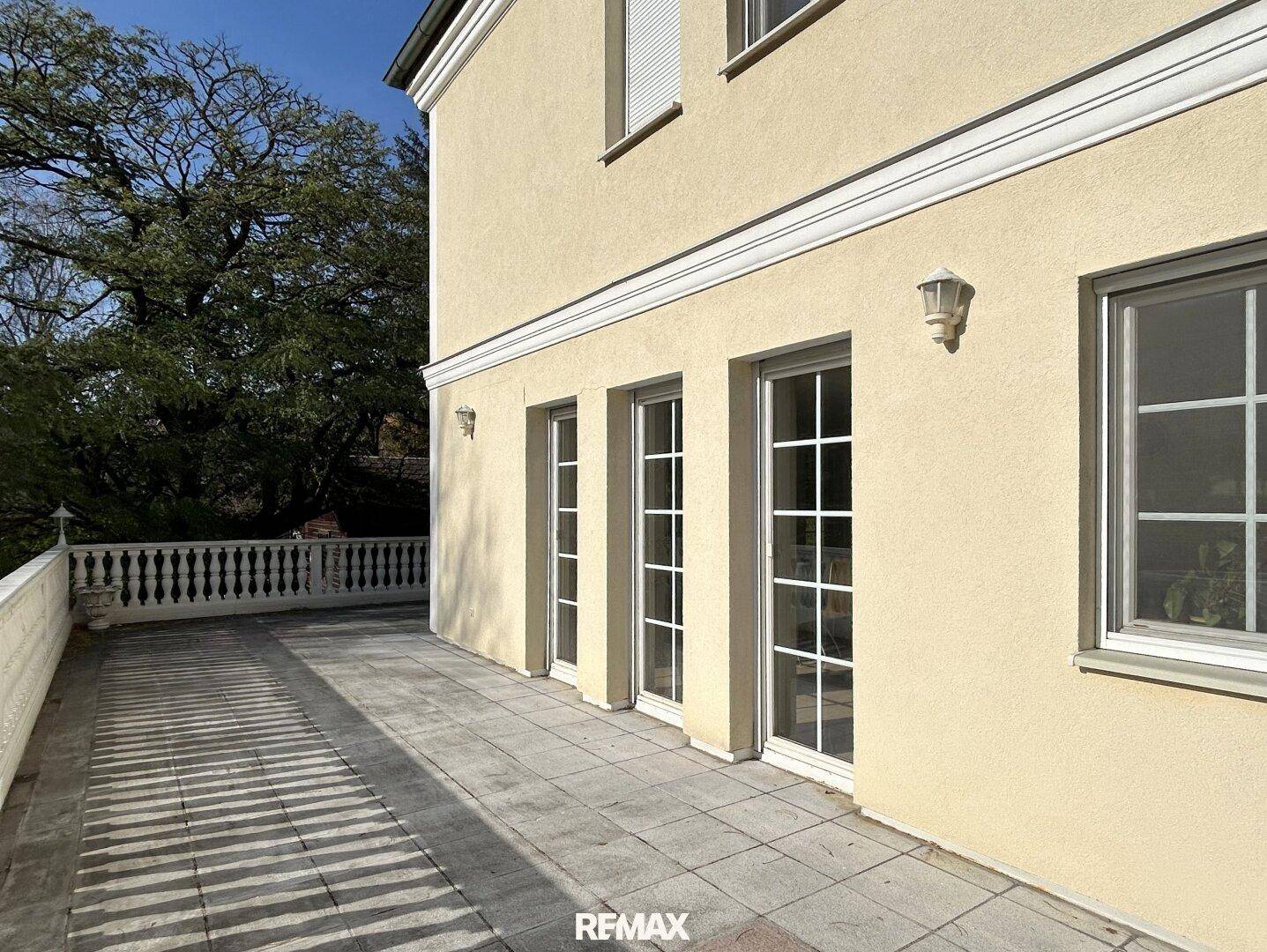 Sonniger Terrassenbereich mit mehreren Zugängen zum Haus und Blick ins Grüne.