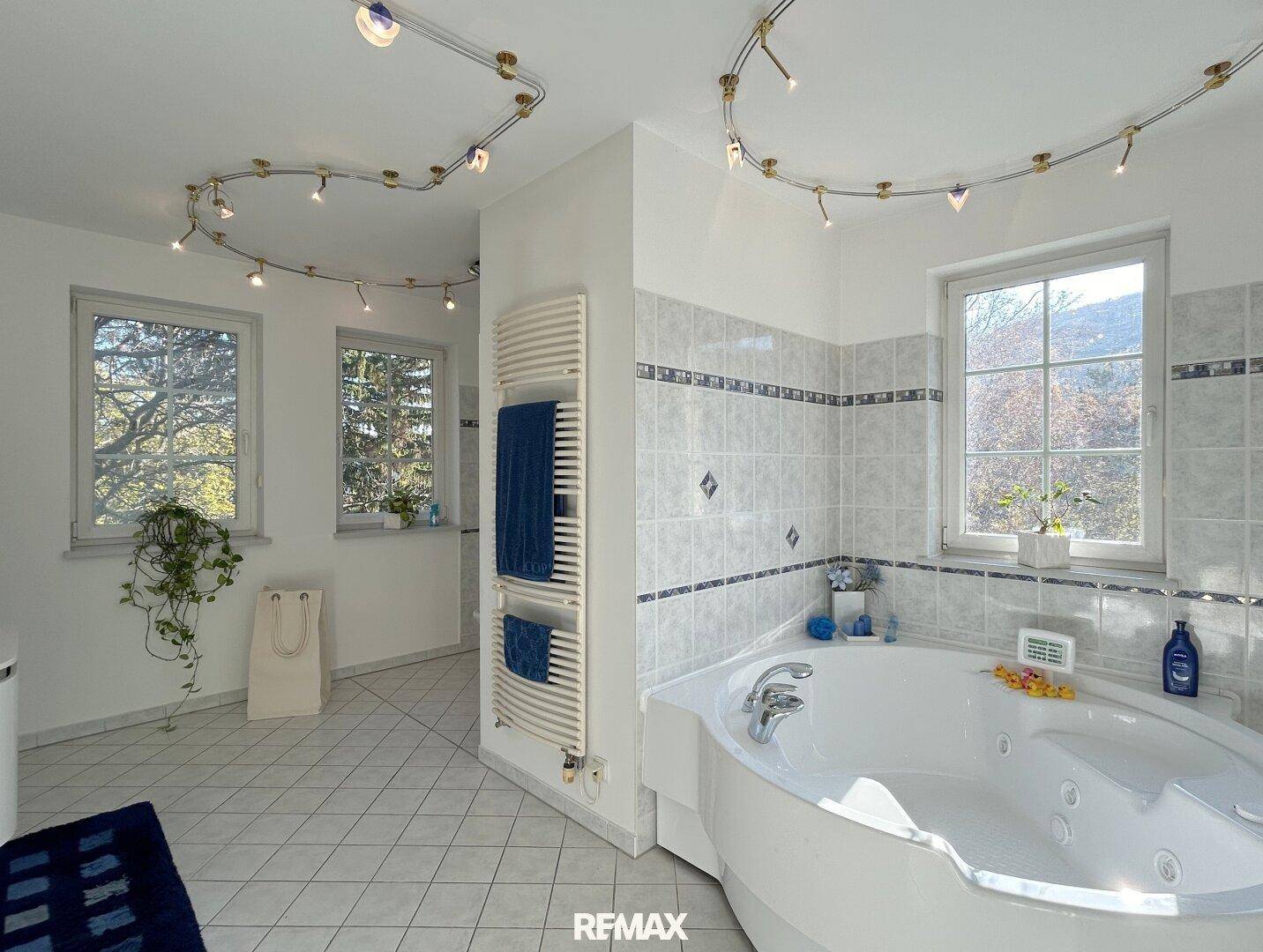 Helles Badezimmer mit Whirlpool, beheiztem Handtuchhalter und Fenstern.