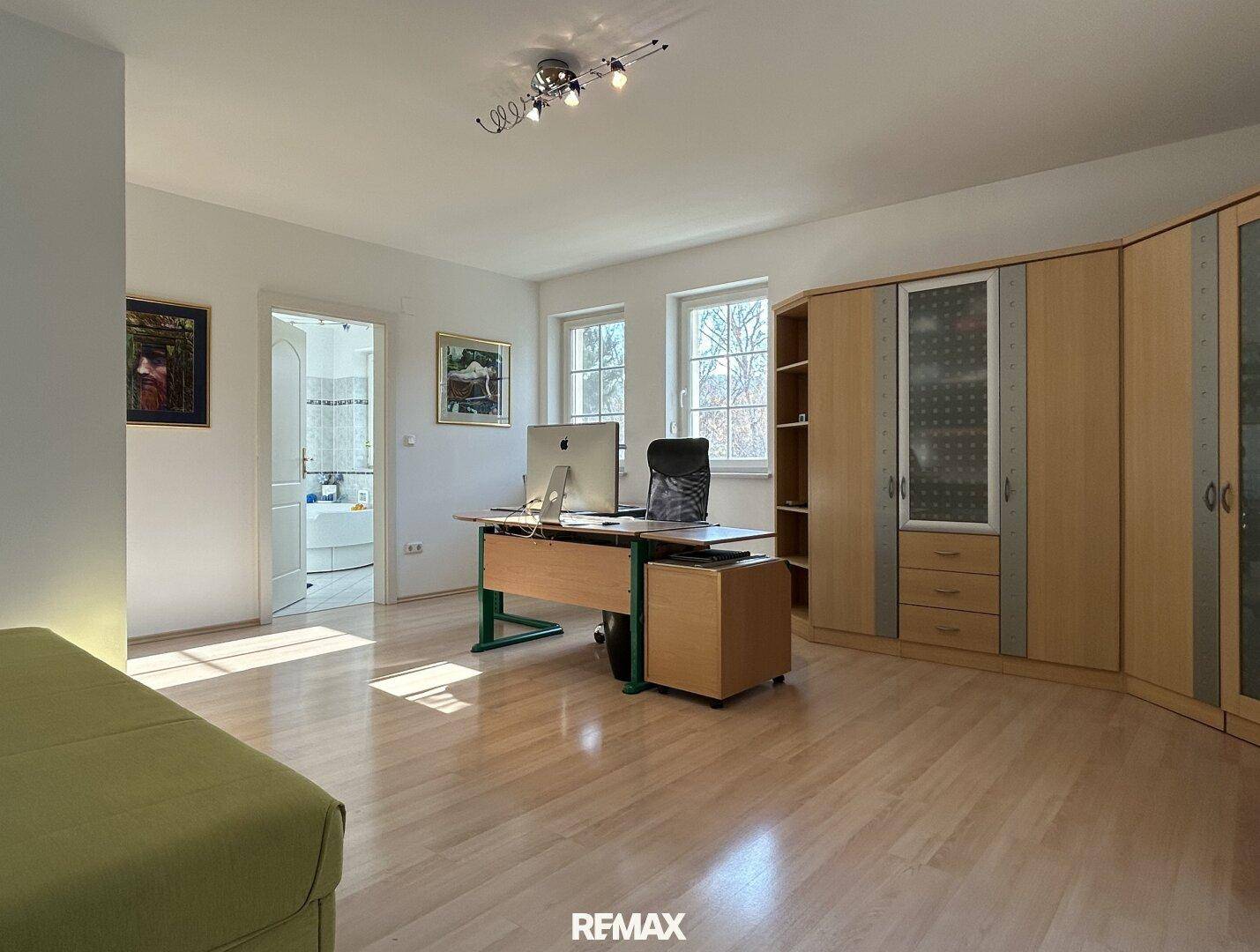 Helles Arbeitszimmer mit Holzschränken, Schreibtisch und Zugang zu einem Badezimmer.