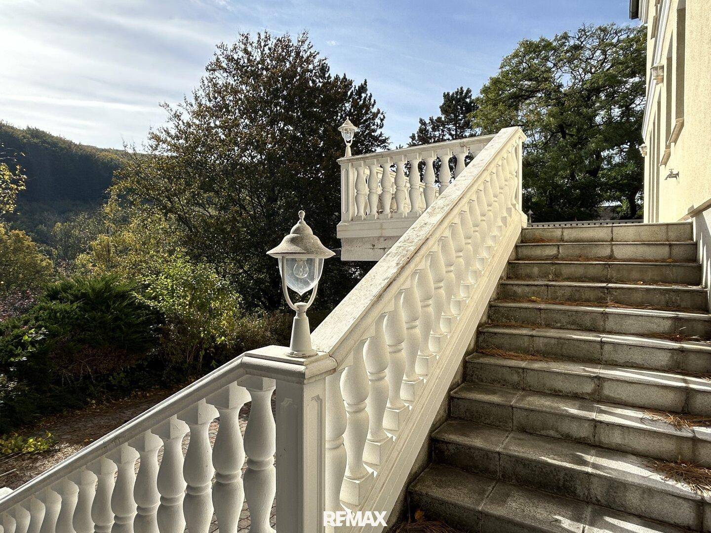 Klassische Steintreppe mit dekorativer Balustrade und Laternen, umgeben von Natur.