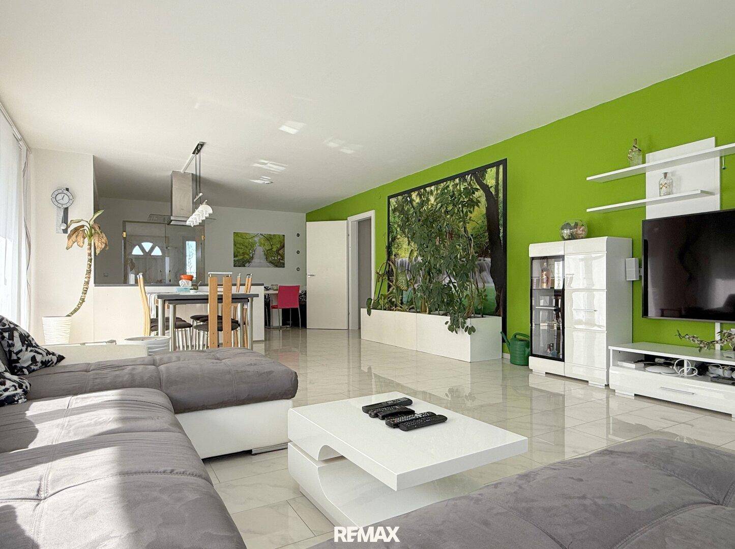 Geräumiger Wohn-Essbereich mit grüner Akzentwand, Fliesenboden und großem Sofa.