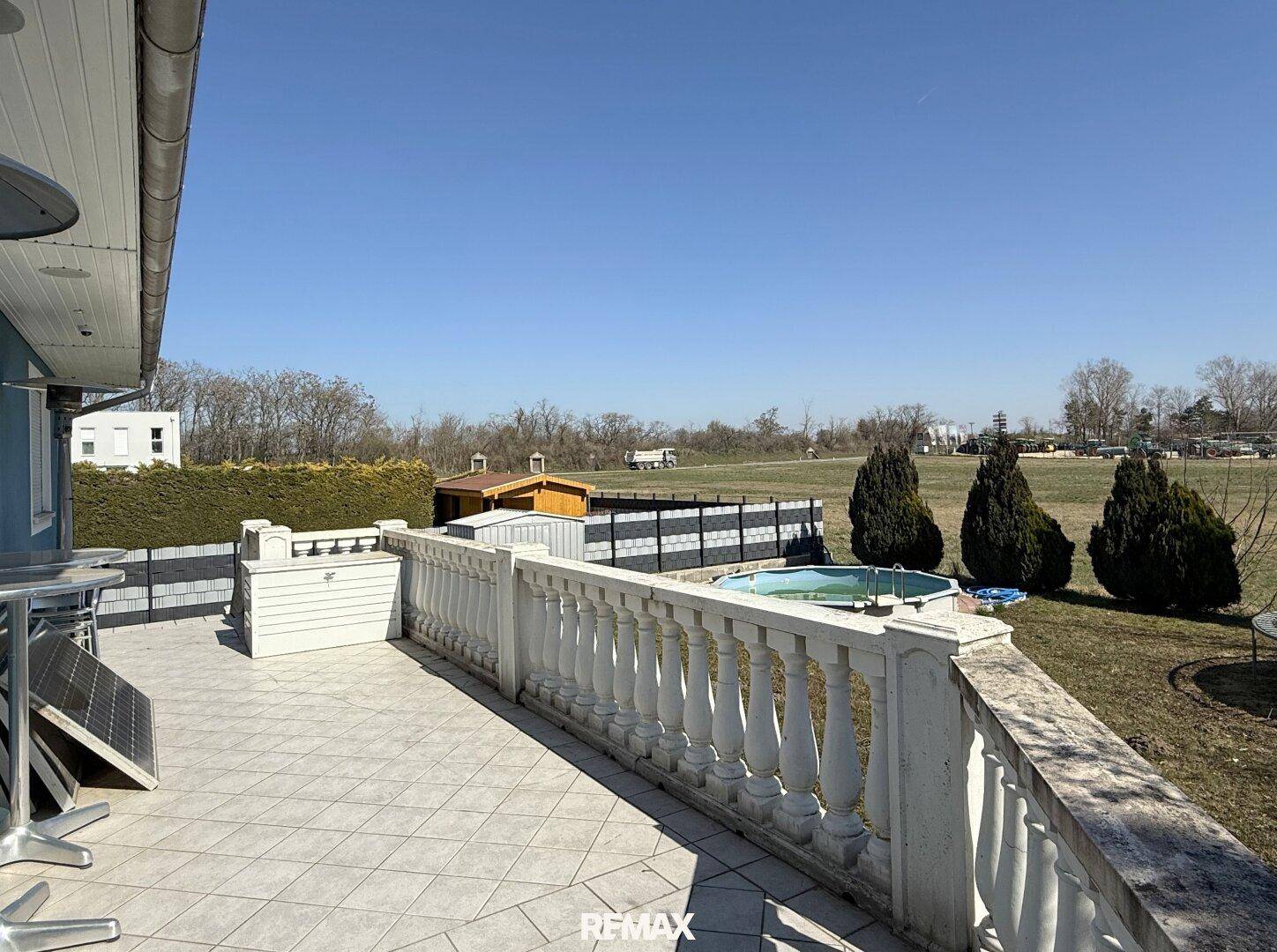 Weitläufige Terrasse mit Balustrade, Blick ins Grüne und einem kleinen Pool im Garten.