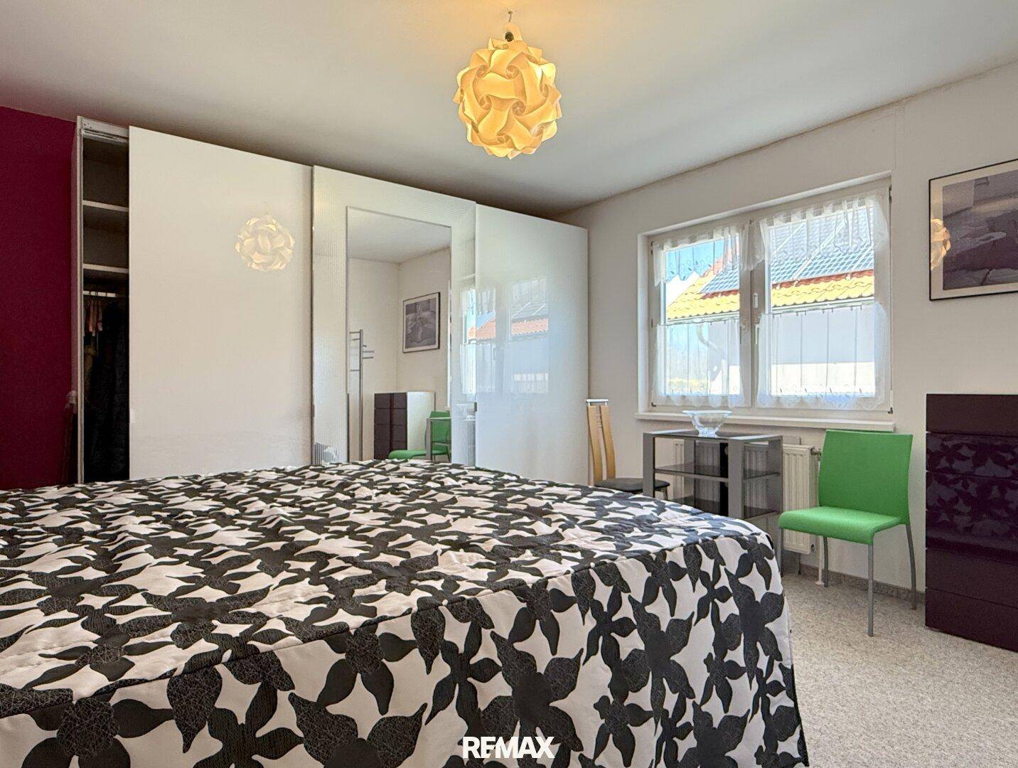 Helles Schlafzimmer mit großem Bett, Spiegelschränken und Fenster mit Vorhängen.