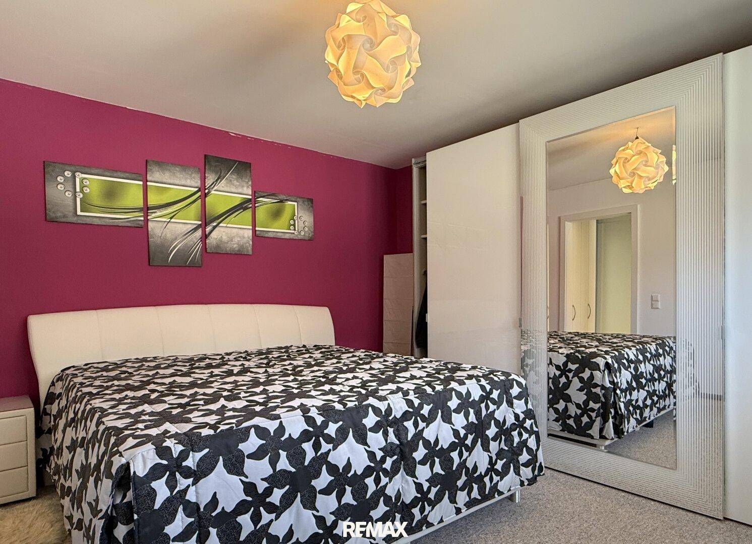 Schlafzimmer mit Doppelbett, pinker Wand und moderner Kunst an der Wand.