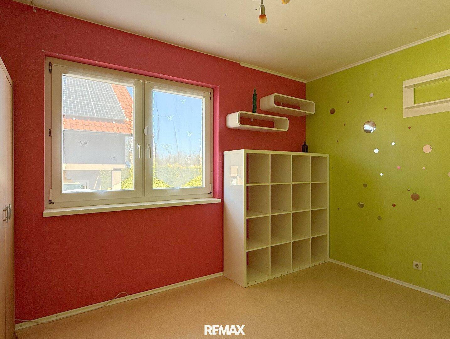 Kinderzimmer mit bunten Wänden, Regal und Blick auf das Nachbardach mit Solaranlage.