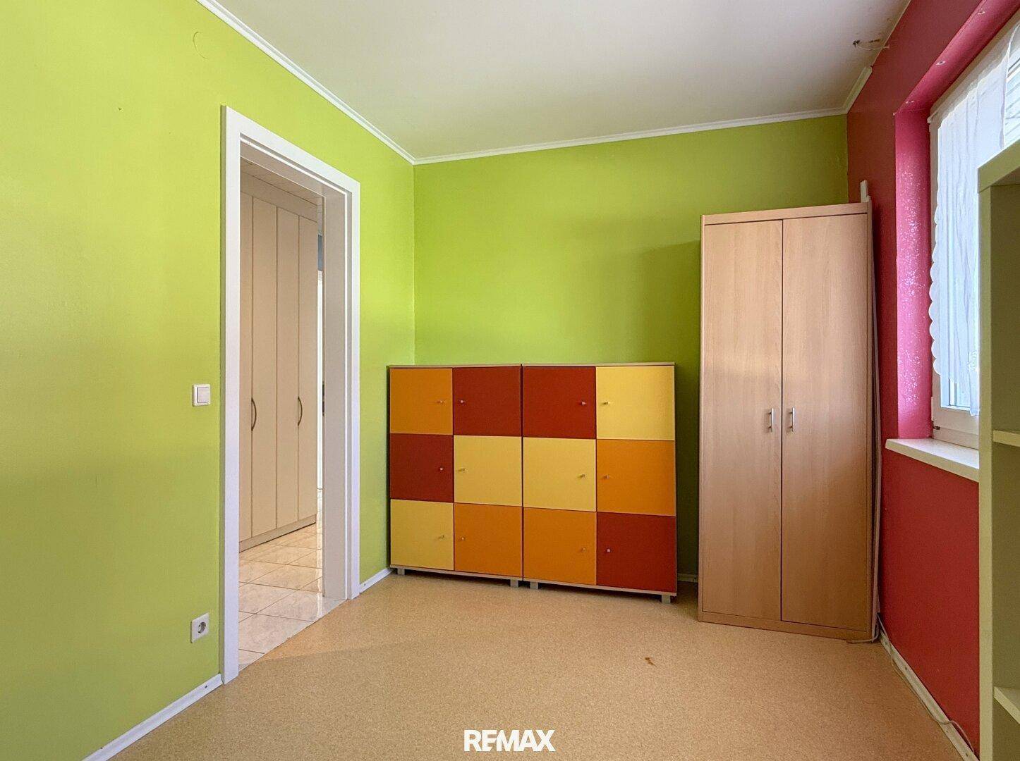Buntes Zimmer mit Schrank, Regal und Zugang zu einem weiteren Raum.
