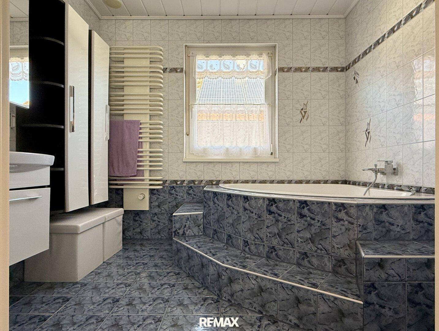 Badezimmer mit großer Eckbadewanne, blauen Fliesen und beheiztem Handtuchhalter.
