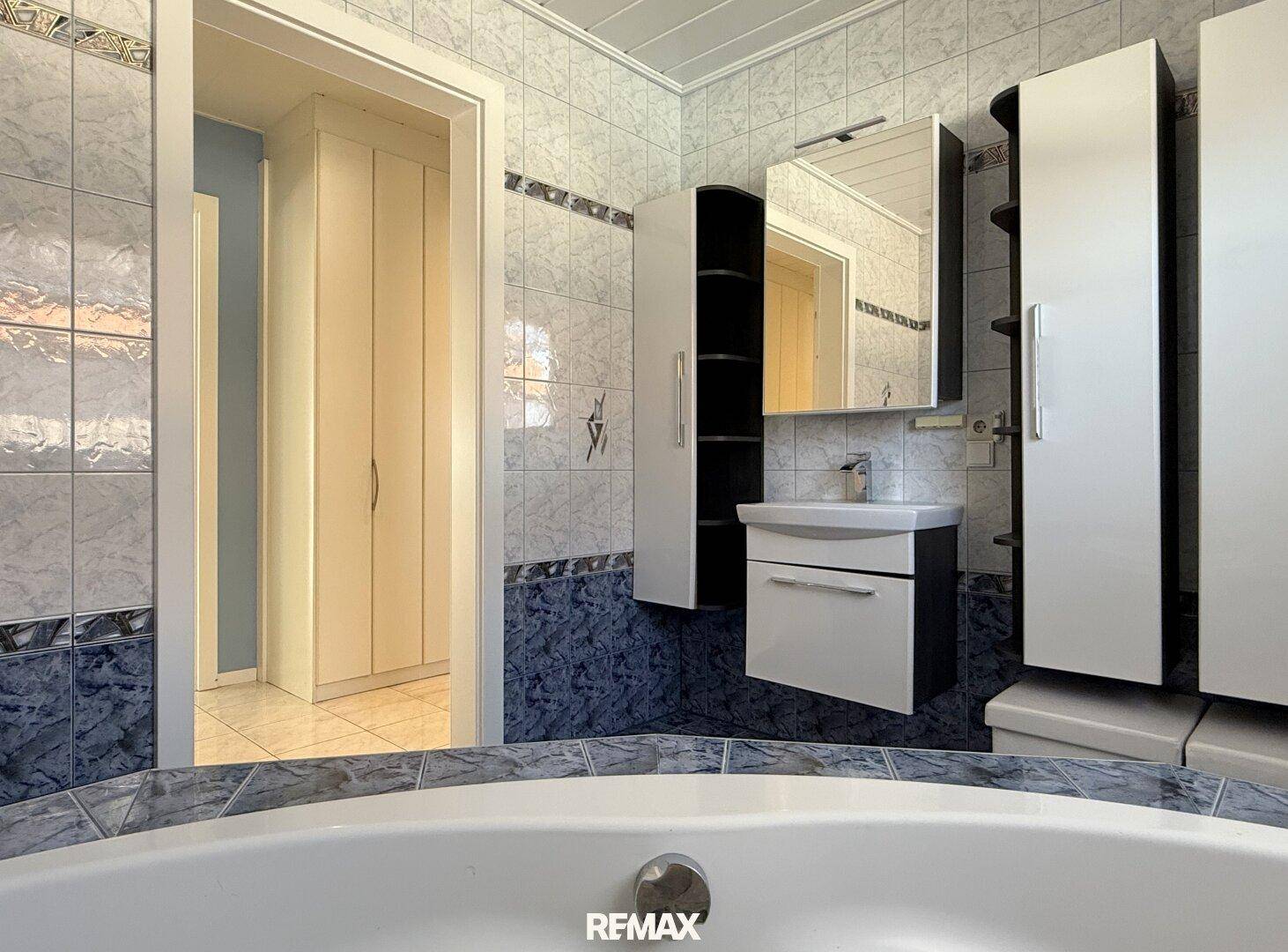 Badezimmer mit Waschbecken, Spiegelschrank und Blick auf die Eckbadewanne.