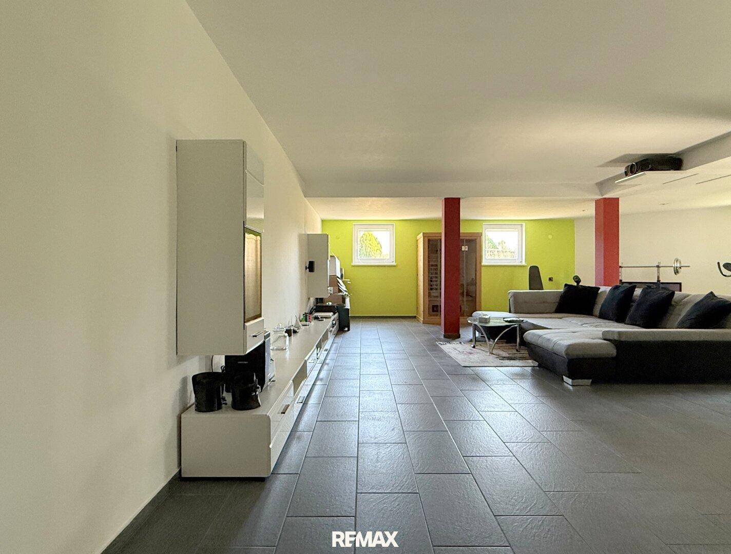 Großer Hobbyraum im Keller mit Sofa, Fitnessgeräten und Fliesenboden.
