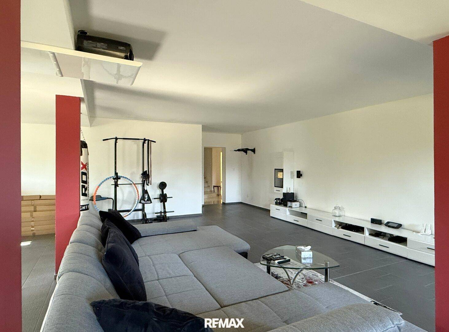 Geräumiger Wohnbereich mit großem Sofa, Fliesenboden und integriertem Fitnessbereich, ideal für Entspannung und Training.