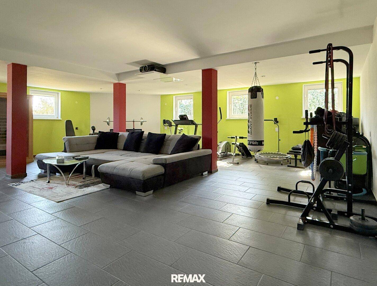 Großer, heller Wohn- und Fitnessraum mit verschiedenen Trainingsgeräten, Sofa und grünen Akzentwänden.