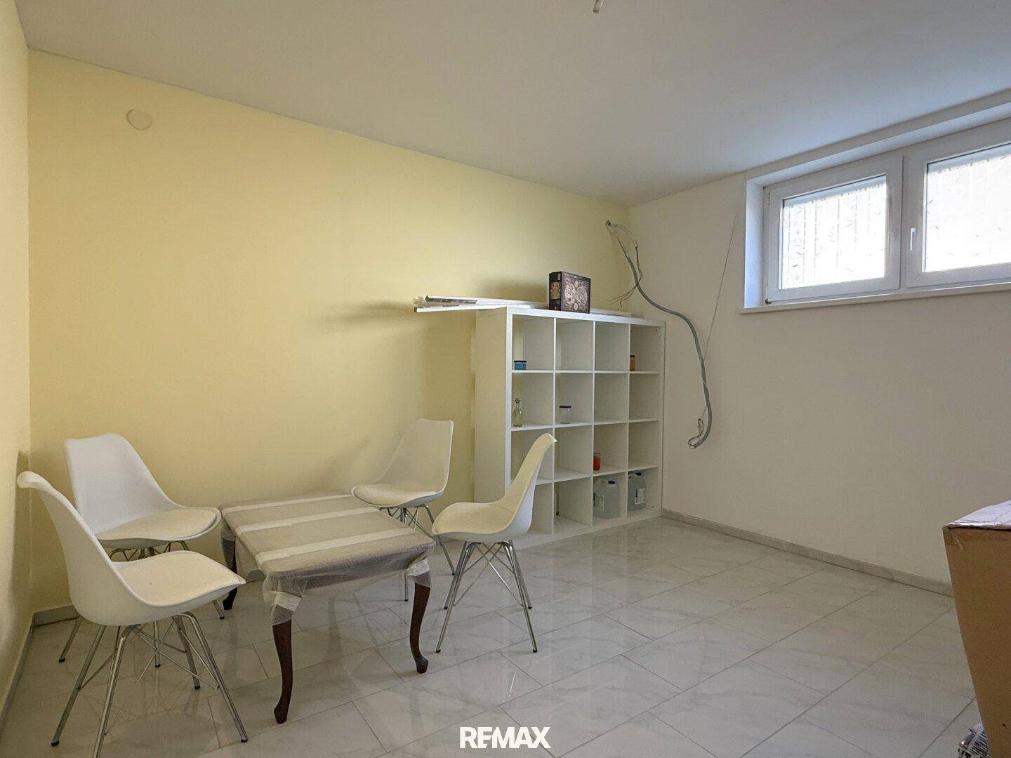 Heller Raum mit gelben Wänden, weißen Fliesen und einem kleinen Tisch mit Stühlen, ideal als Gäste- oder Arbeitszimmer.