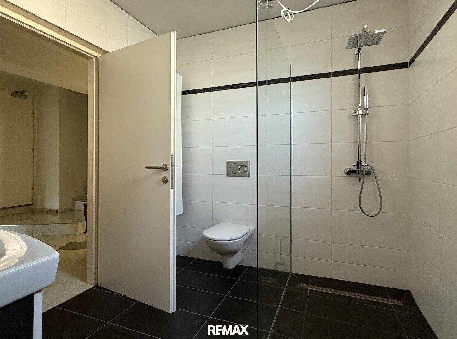 Modernes Badezimmer mit begehbarer Dusche, Regendusche und wandhängendem WC, ausgestattet mit dunklen Bodenfliesen.