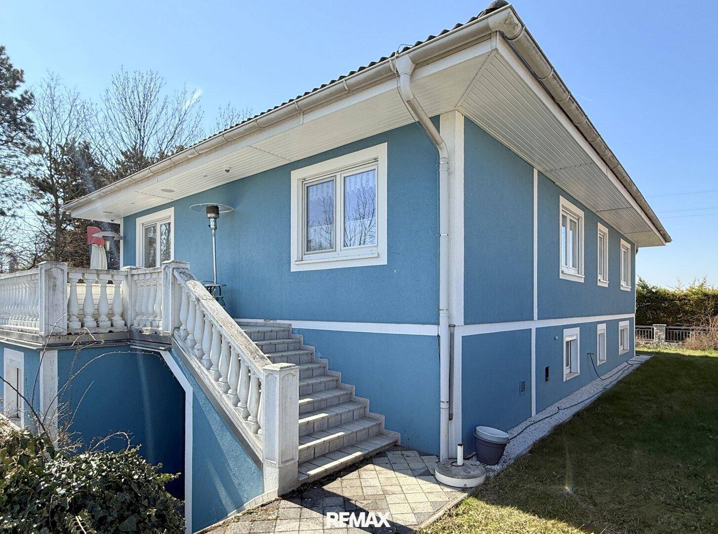 Blau gestrichenes Haus mit weißer Balustrade und Außentreppe unter strahlend blauem Himmel.