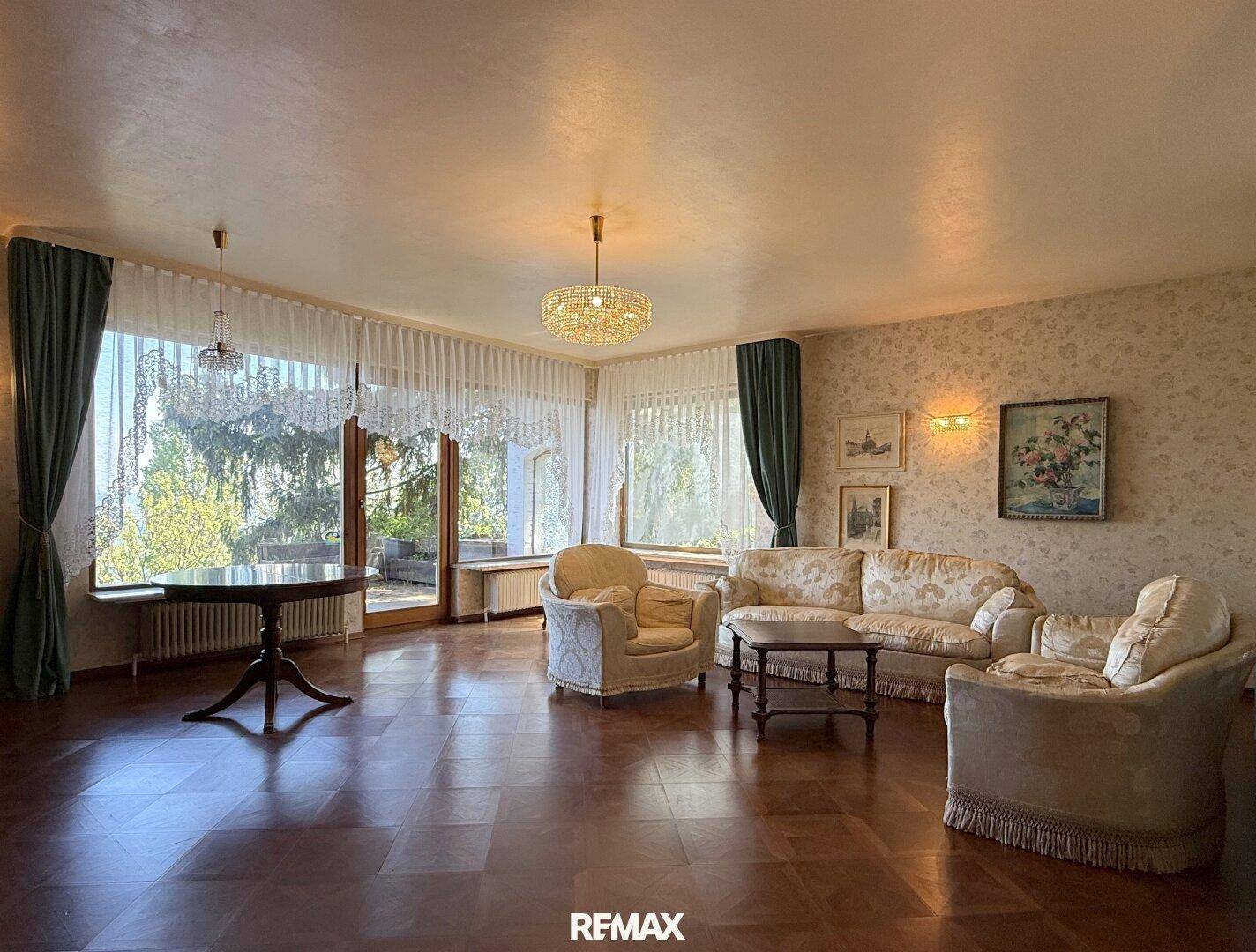 Helles Wohnzimmer mit klassischer Einrichtung, Parkettboden und großen Fenstern mit Ausblick ins Grüne.