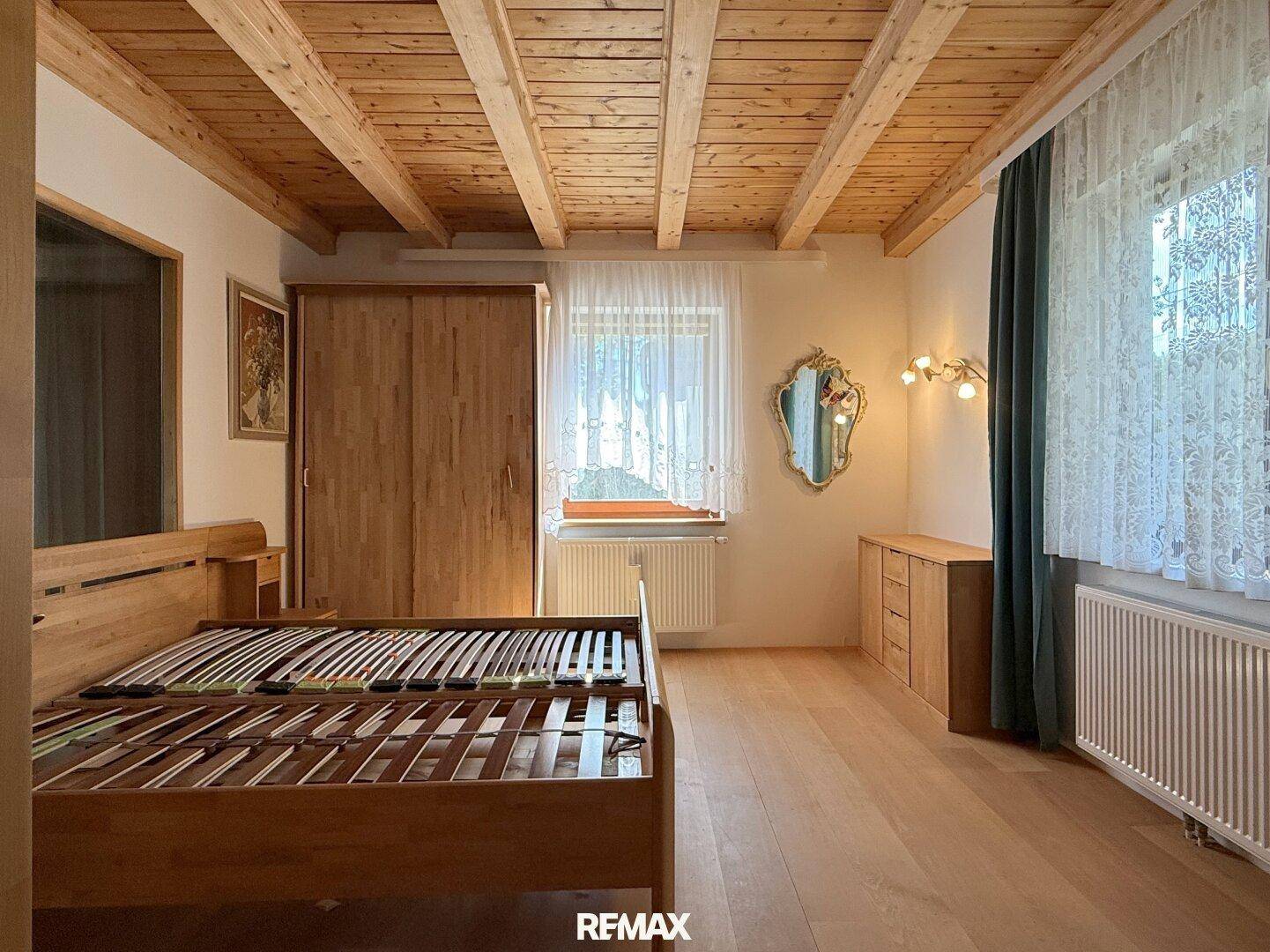 Schlafzimmer mit Holzbalkendecke, Parkettboden und einem großen Fenster für viel Tageslicht.