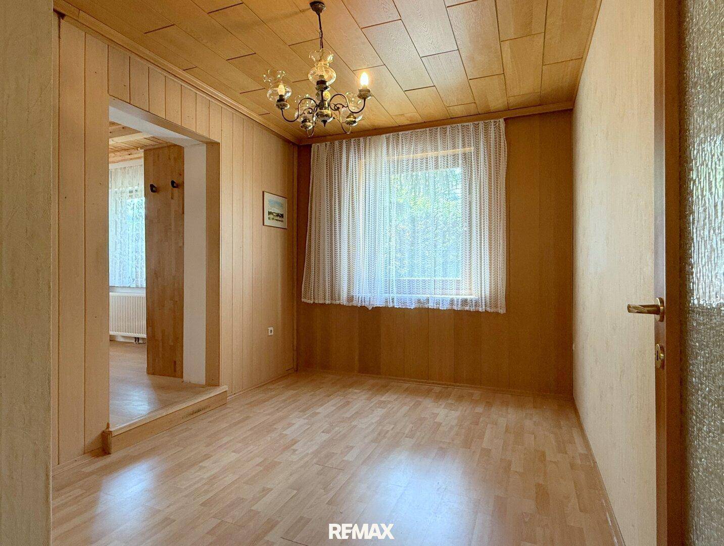 Kleiner Raum mit Holzvertäfelung, Laminatboden und einem Fenster, das Tageslicht hereinlässt.