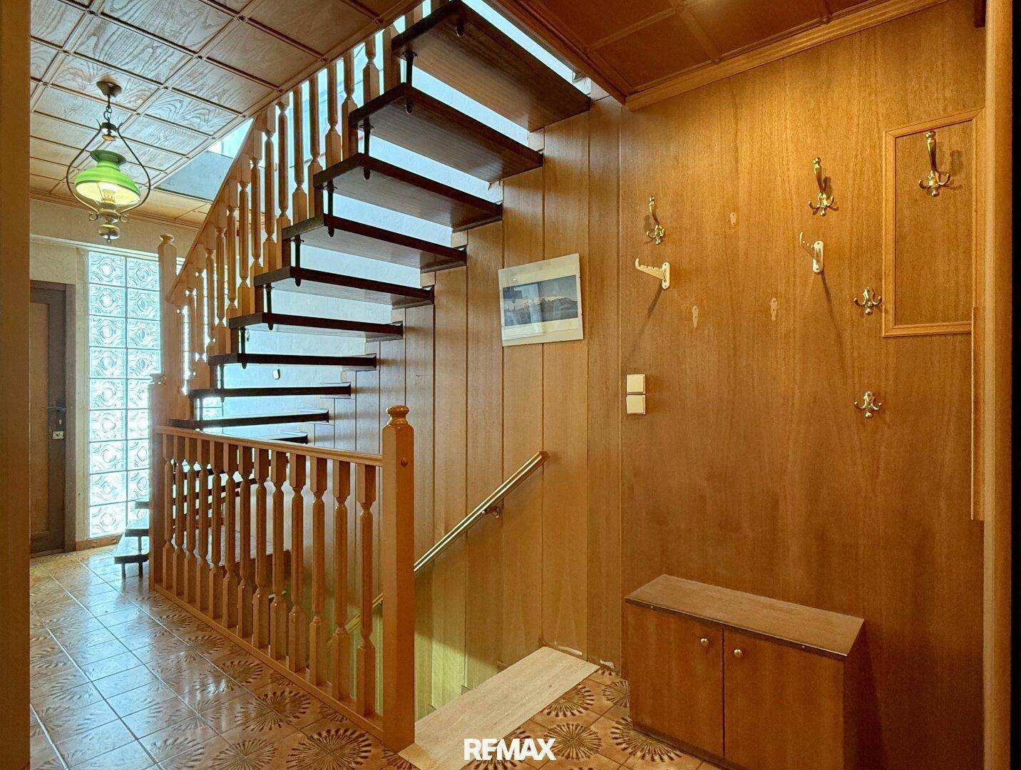 Flur mit Holzvertäfelung, Holztreppe und gemusterten Fliesen, die zum Obergeschoss führt.