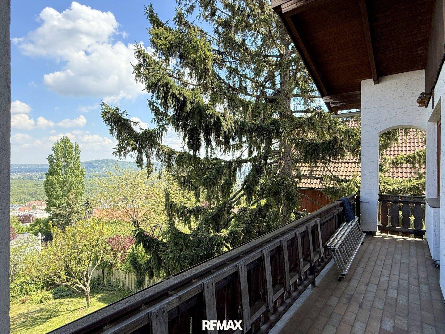 Langer Balkon mit Holzbalkonbrüstung und Fliesenboden, bietet einen weiten Blick ins Grüne.