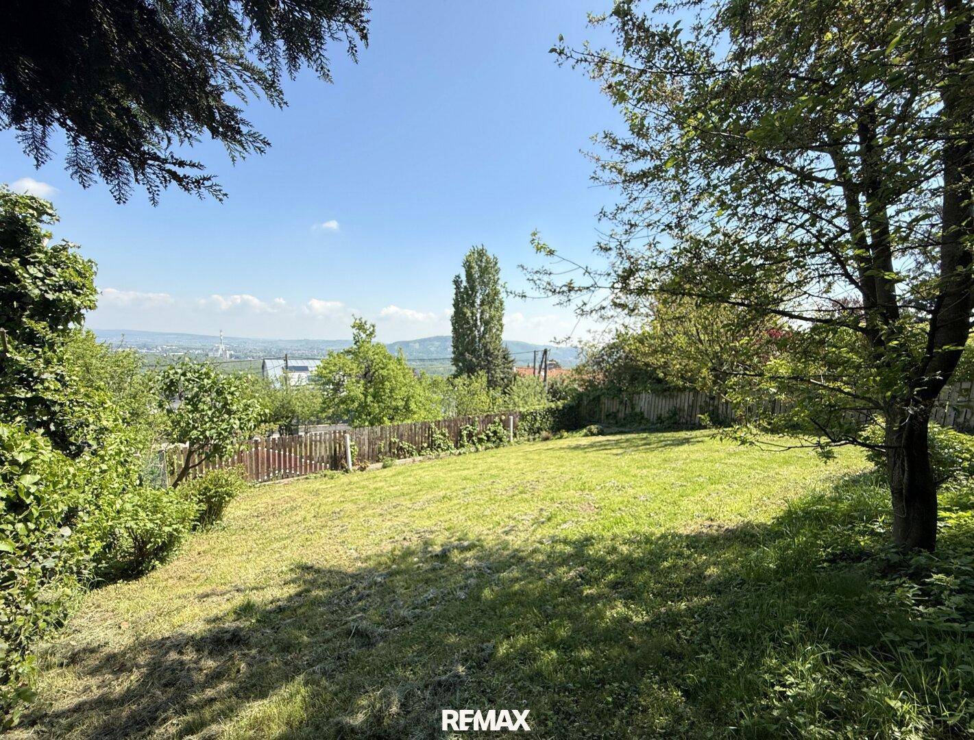 Weitläufiger Garten mit Rasenfläche und Blick auf die umliegende Landschaft unter blauem Himmel.