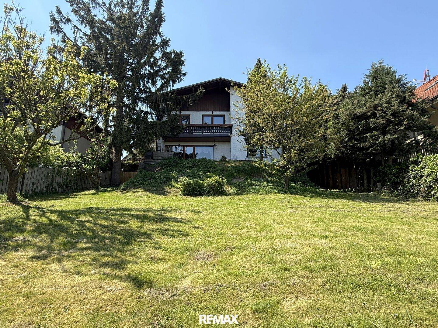 Rückansicht des Hauses mit großem Garten und Balkon, umgeben von viel Grün.