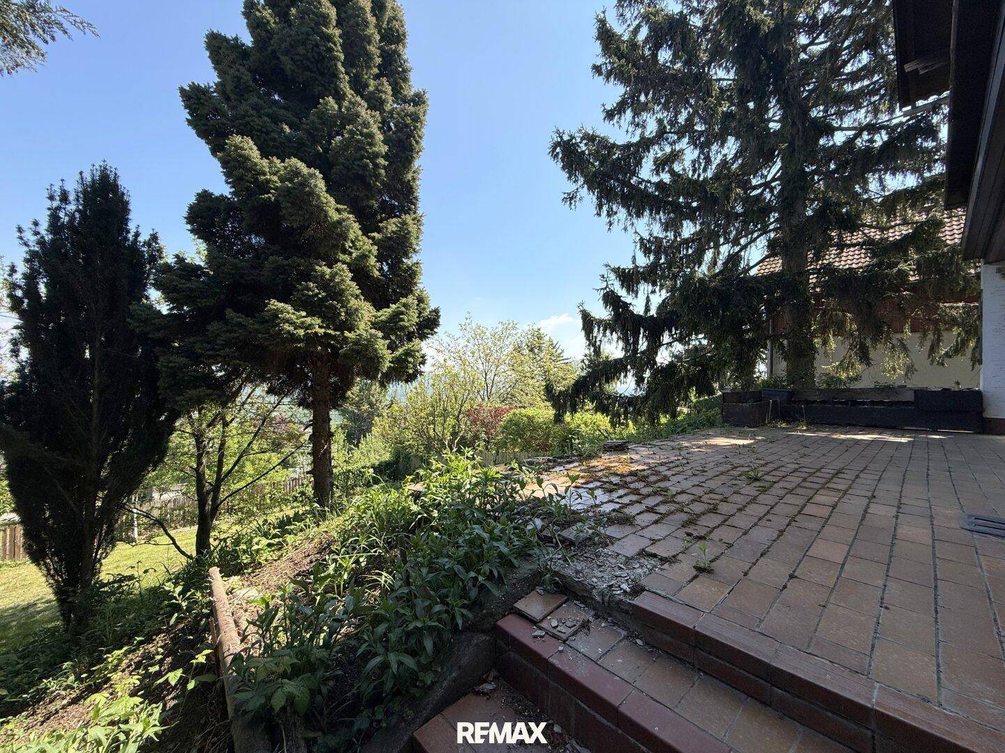 Große gepflasterte Terrasse mit Stufen, umgeben von Bäumen und üppigem Grün, bietet einen weiten Ausblick.