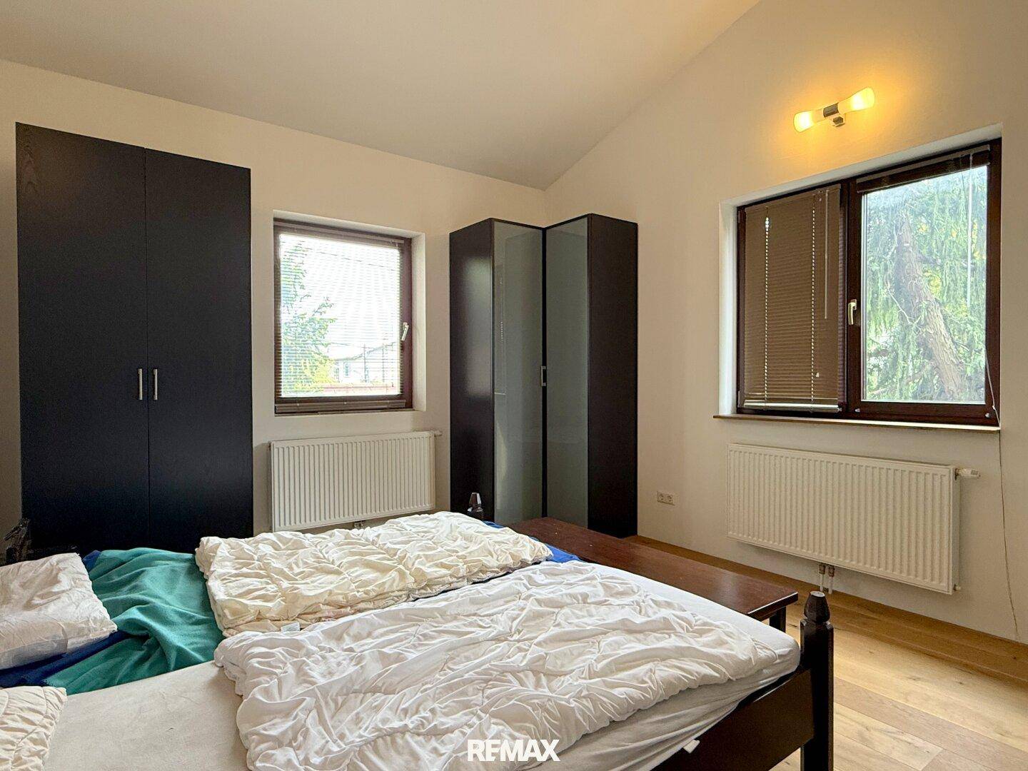 Schlafzimmer mit Holzboden, dunklen Schränken und Fenstern mit Jalousien für Privatsphäre.