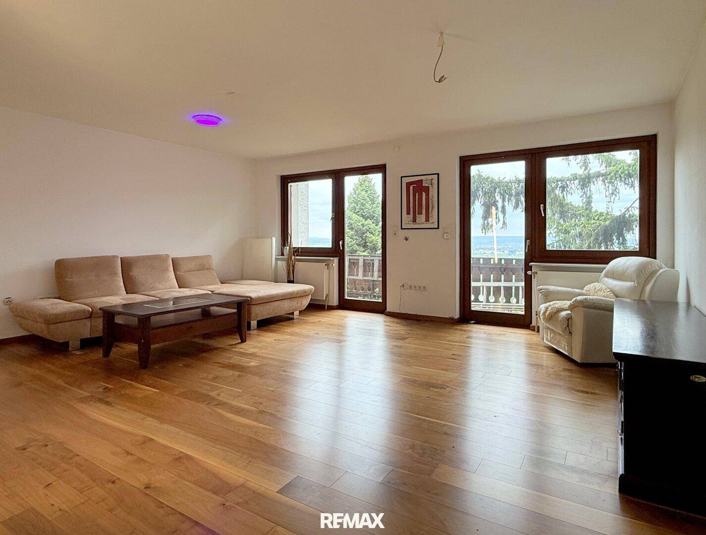 Geräumiges Wohnzimmer mit Holzboden, bequemer Couch und Fenstern, die viel Licht hereinlassen.