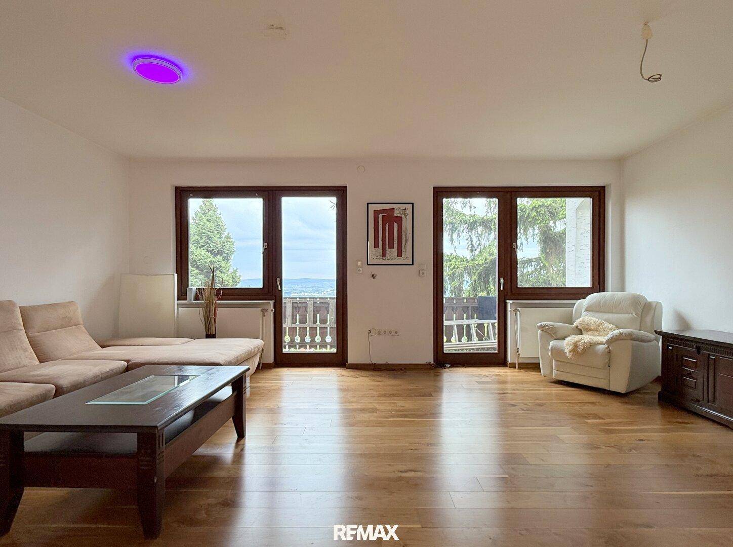 Wohnzimmer mit Holzboden, moderner Couch und großen Fenstern mit Blick auf die Umgebung.